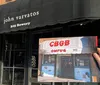 A person is posing with an open book that shows a photo of an individual wearing a New York City shirt seemingly standing in front of the same building that appears in the background