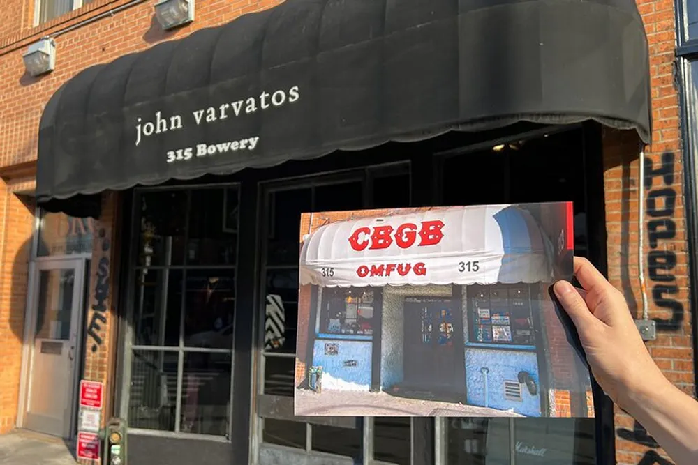 A person is holding an image of the iconic facade of the CBGB music club in front of the current John Varvatos store which now occupies the same location