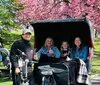 Three people are smiling while sitting in a pedicab in a park with autumn foliage in the background