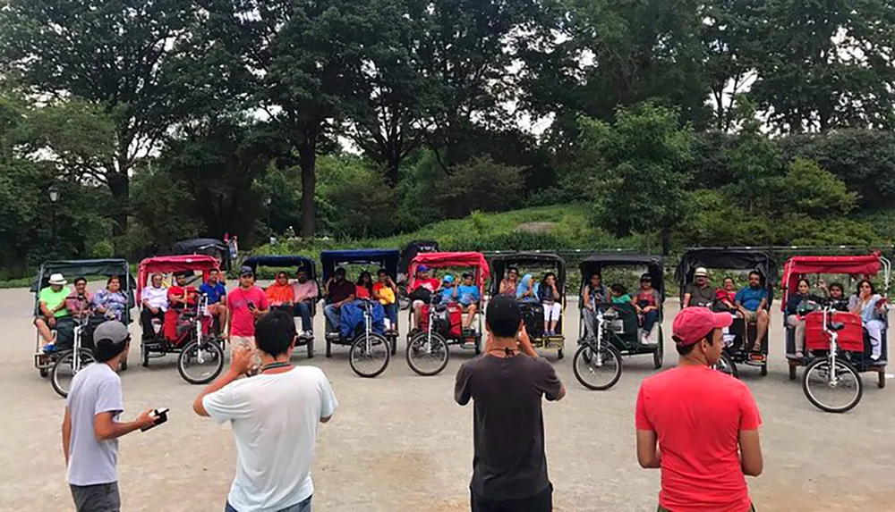 A group of people on colorful pedicabs are posed for a photo in a park-like setting while others stand in front observing