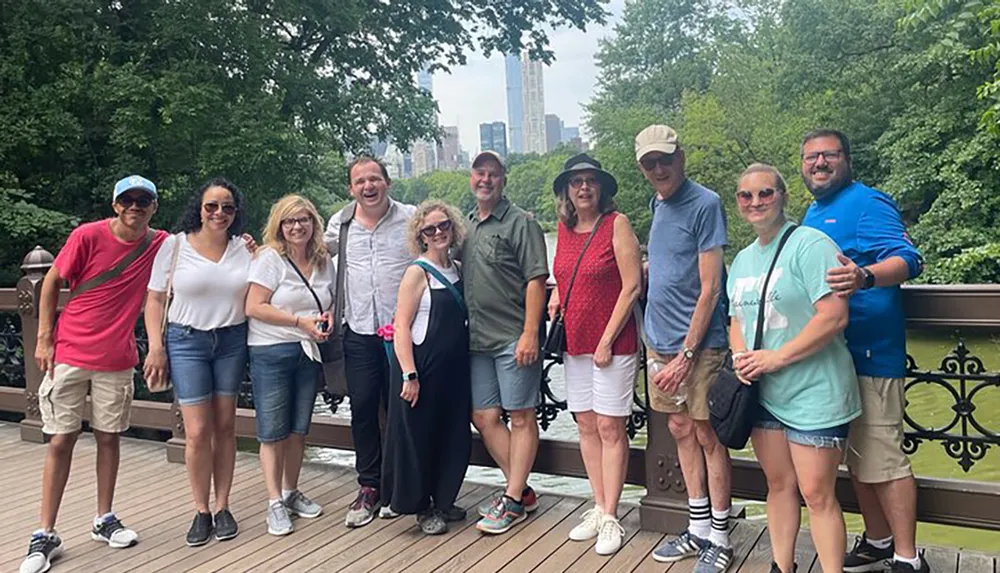 A group of people are smiling for a photo on a bridge with greenery and the skyline of a city in the background