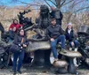 A group of people is posing joyfully with raised arms in front of a fountain in a park on a sunny day