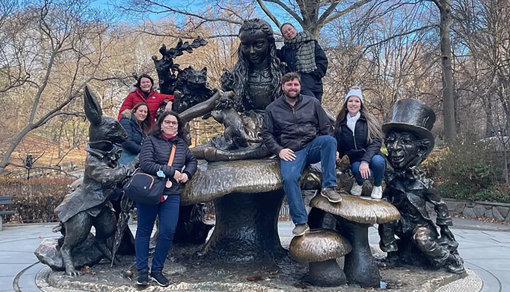 A group of people is posing with a whimsical bronze sculpture of storybook characters in a park-like setting