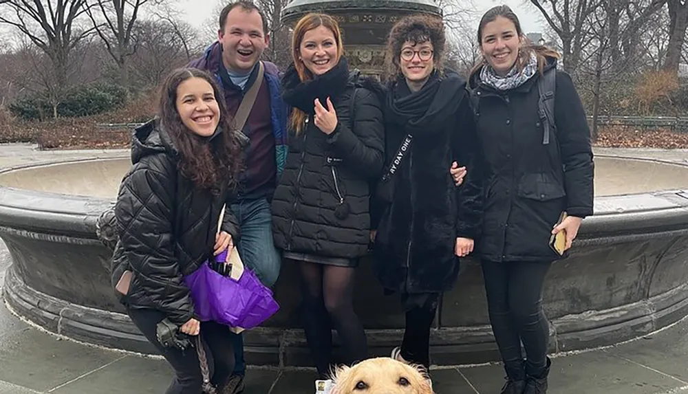 Five people are posing for a photo with smiles while a dogs head is humorously photobombing the picture at the bottom