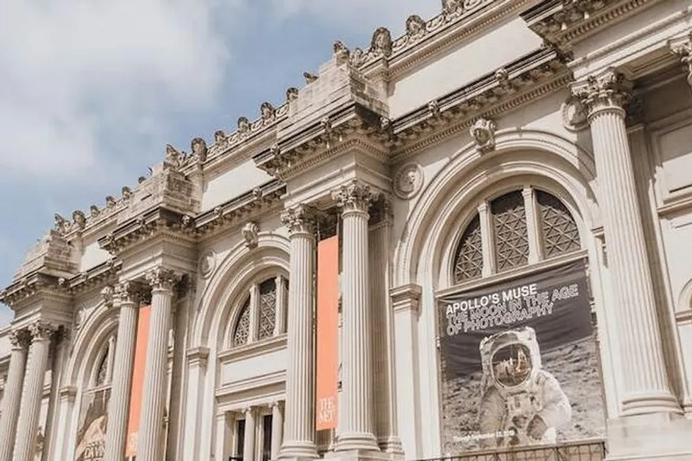 The image shows the ornate facade of a classical-style building with banners promoting an exhibit called Apollos Muse The Moon in the Age of Photography