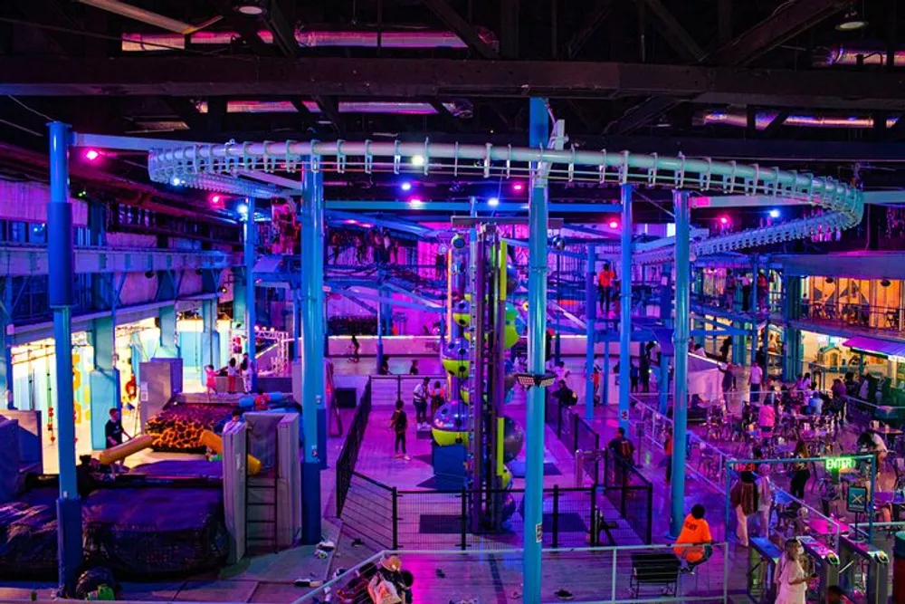 The image shows a vibrant indoor amusement park with various attractions and colorful lighting capturing a lively atmosphere of recreation and entertainment