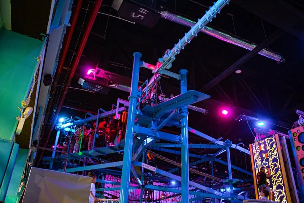 The image shows an indoor entertainment space with colorful neon lighting and what appears to be a multi-level adventure or obstacle course