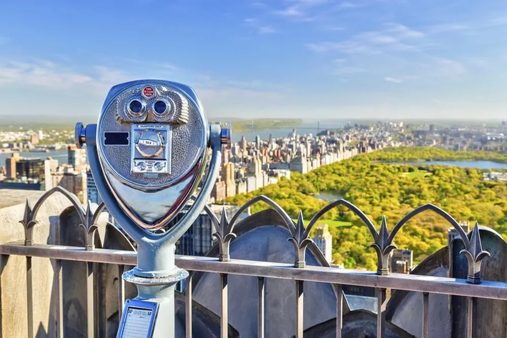 A coin-operated binocular viewer stands overlooking a panoramic aerial view of Central Park and the cityscape beyond