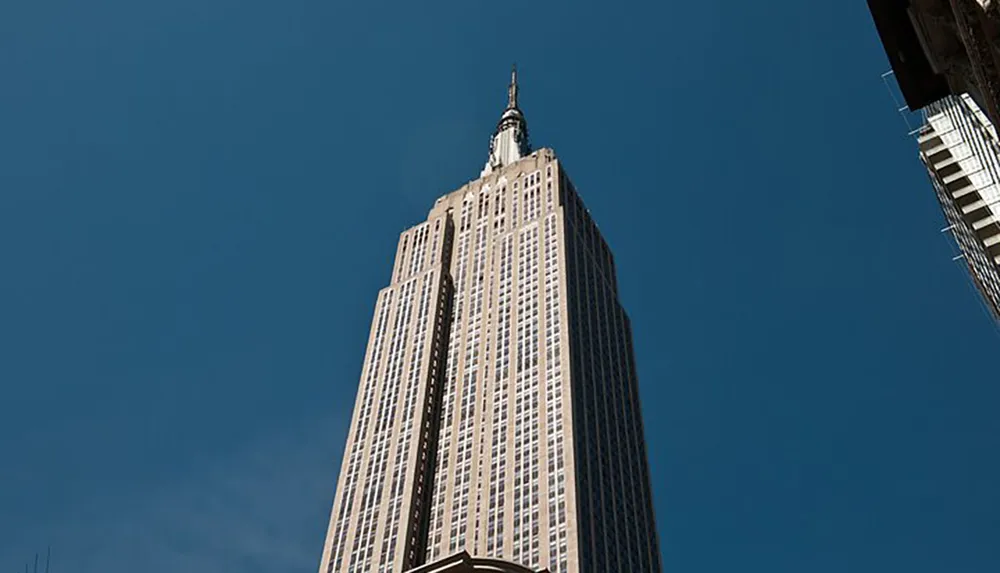 The image captures a towering skyscraper soaring into a clear blue sky flanked by the edges of other buildings