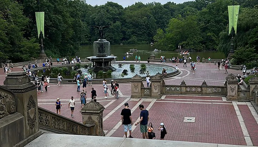 The image shows a bustling scene at an ornate fountain and terrace with people walking chatting and enjoying a day at a park with some boats visible in the background on a pond surrounded by trees