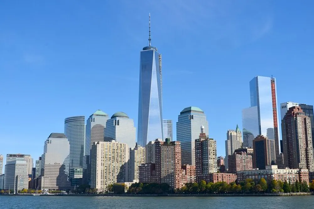 The image depicts the Lower Manhattan skyline with the One World Trade Center dominating the view under a clear blue sky