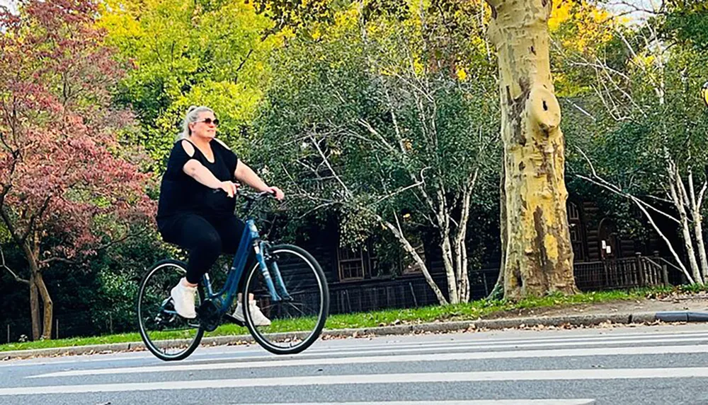 A person is biking along a street with lush greenery and colorful trees in the background