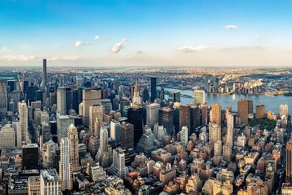 An aerial view showcases a dense array of skyscrapers and buildings in a bustling metropolis with a wide river visible in the background