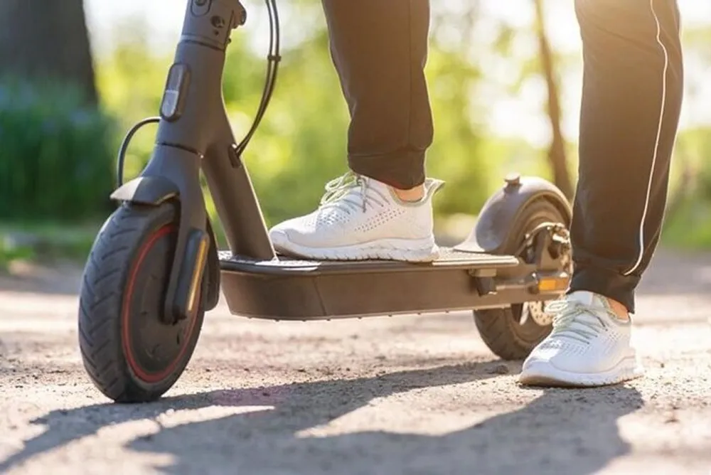 A person stands on an electric scooter poised to ride on a sunlit path