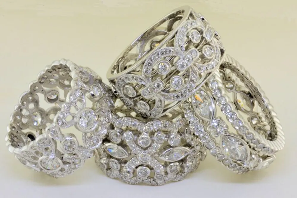 The image shows a stack of intricate silver bracelets adorned with multiple sparkling gemstones