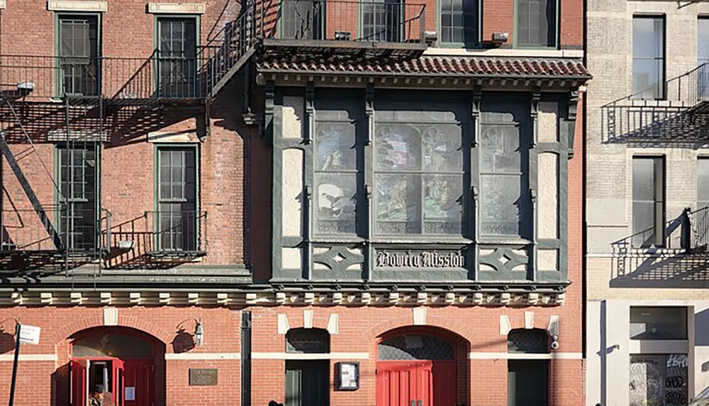 The image shows a close-up of a building faade with ornate window designs and the words Bowery Mission displayed on its upper part suggesting it may be a historical or charitable establishment