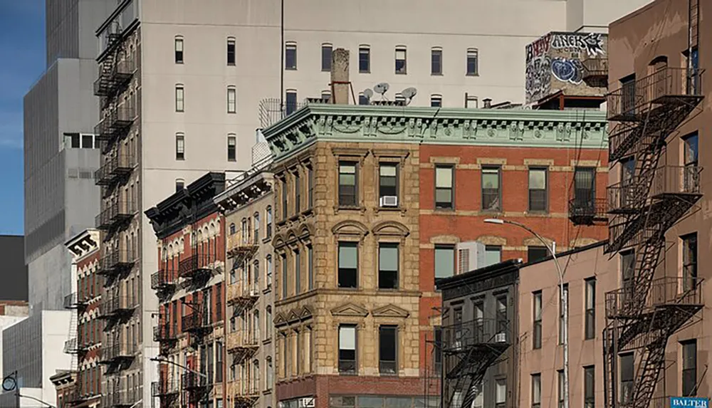 The image depicts a street view of a row of traditional multi-story buildings with fire escapes showcasing a mix of architectural styles under a clear sky