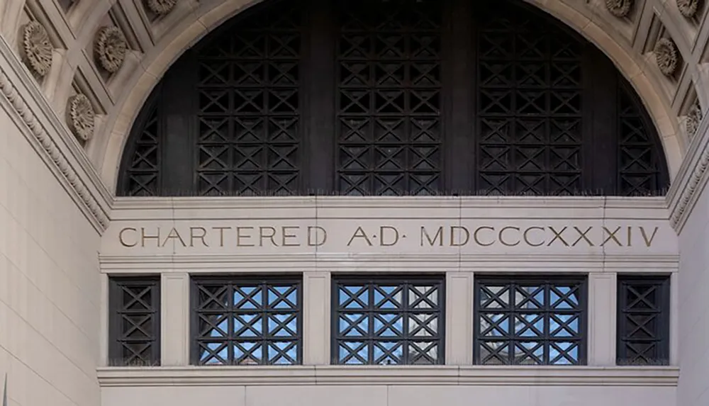 The image shows a close-up of a stone building facade with engraved text CHARTERED AD MDCCCXXIV above a trio of ornate windows set beneath a Gothic arch