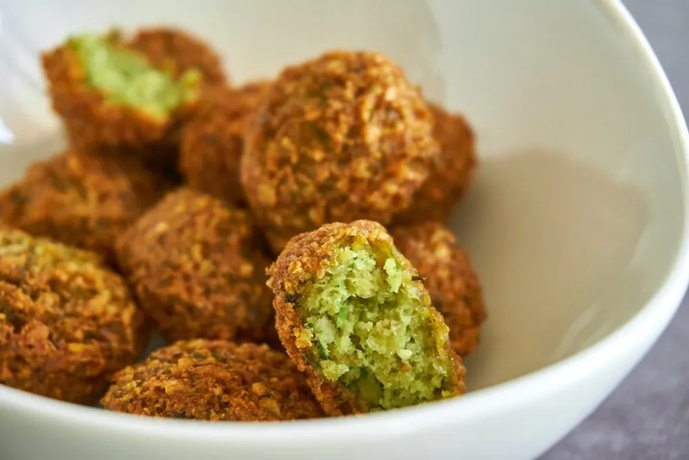 The image shows a bowl of freshly cooked falafel with one split in half to reveal the green herb-infused interior