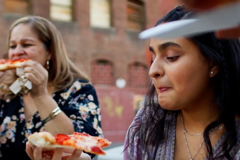 Two women appear to be enjoying slices of pizza outdoors