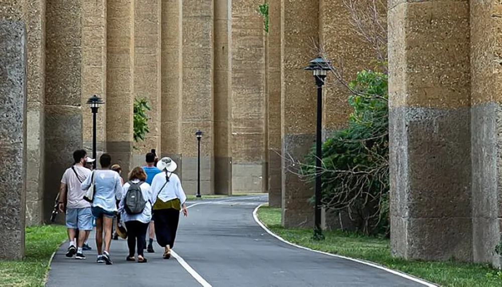 A group of people is walking down a path flanked by tall column-like structures and street lamps