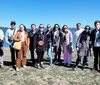 A group of people poses for a photo standing on grass near a body of water under a clear blue sky