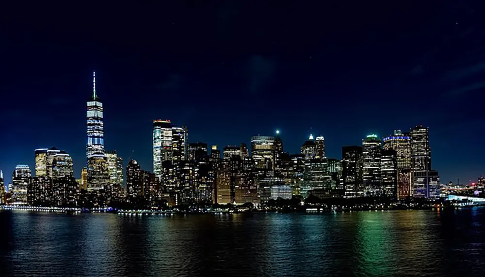 The image features a nighttime skyline view of an illuminated city with tall buildings dominated by a prominent tower reflecting off the water in the foreground against a dark blue sky