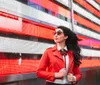 A stylish woman in a red jacket and sunglasses walks confidently in front of a vibrant red LED display