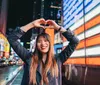 A stylish woman in a red jacket and sunglasses walks confidently in front of a vibrant red LED display