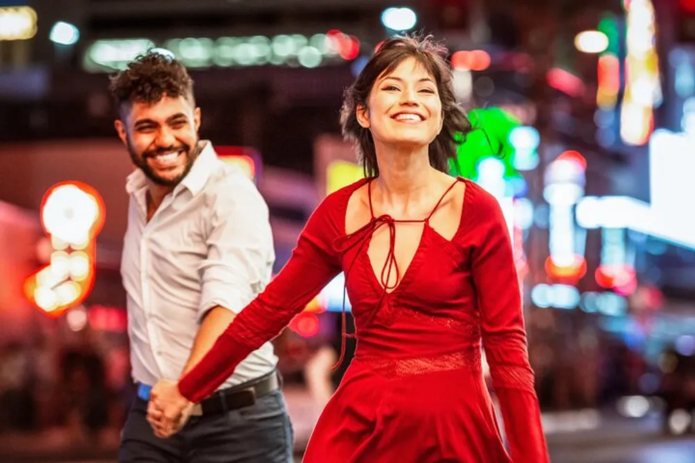 A couple is joyfully dancing on a bustling city street at night surrounded by vibrant lights