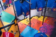 The image shows an indoor playground with colorful floors and scattered soft balls, featuring play structures for children's entertainment.