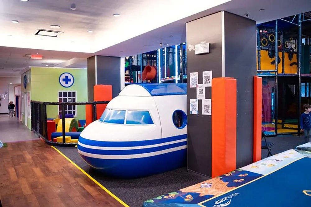 The image shows a colorful indoor play area with a mock airplane cabin and various play structures for children