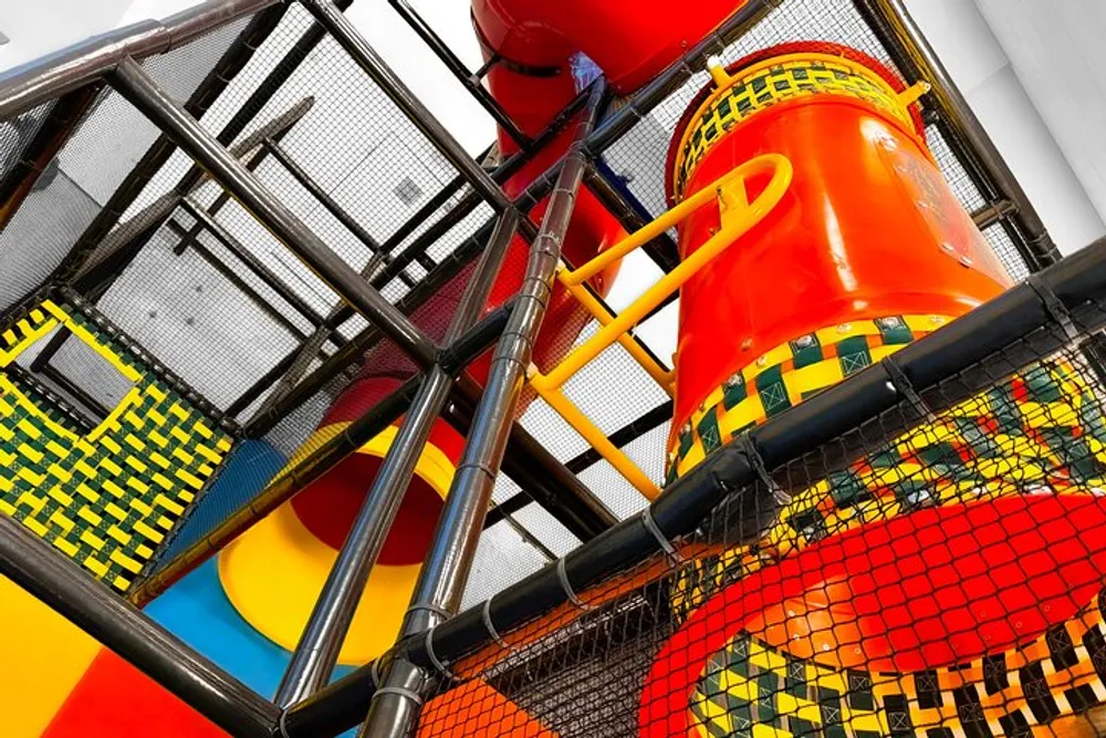 A colorful indoor playground is shown with vibrant tube slides netted climbing areas and padded play structures