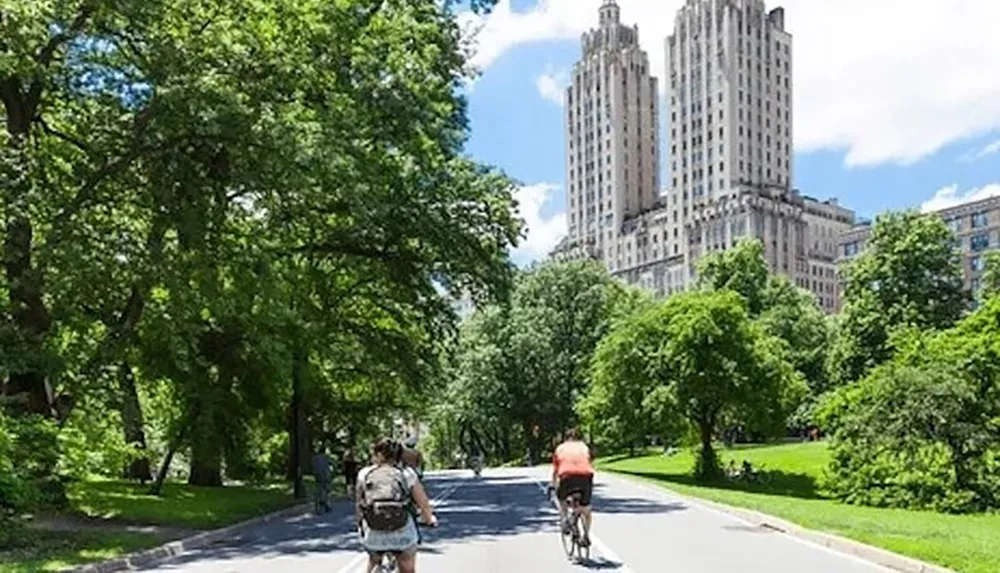 Cyclists and pedestrians enjoy a sunny day on a tree-lined path with an imposing building in the background