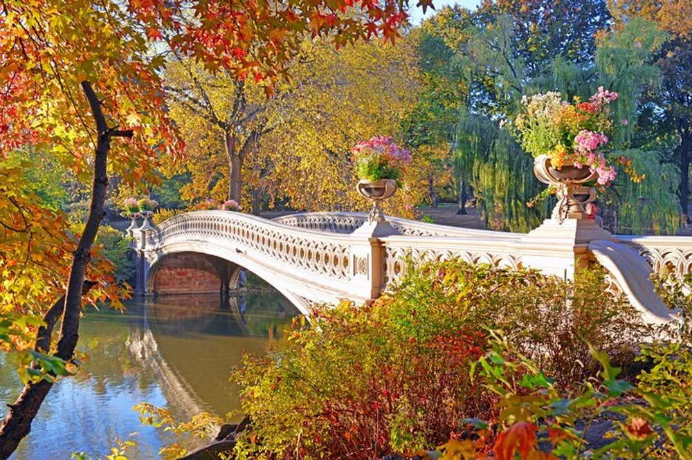 The image features a scenic view of an ornate white bridge adorned with flower pots surrounded by colorful autumn foliage reflecting in the calm water below