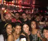 Four friends are posing for a group photo with smiles and thumbs-up gestures seemingly enjoying a good time together in a bar-like setting