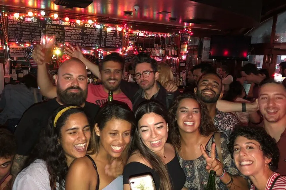 A group of joyful people posing for a selfie in a crowded bar with festive lights and a drinks menu in the background