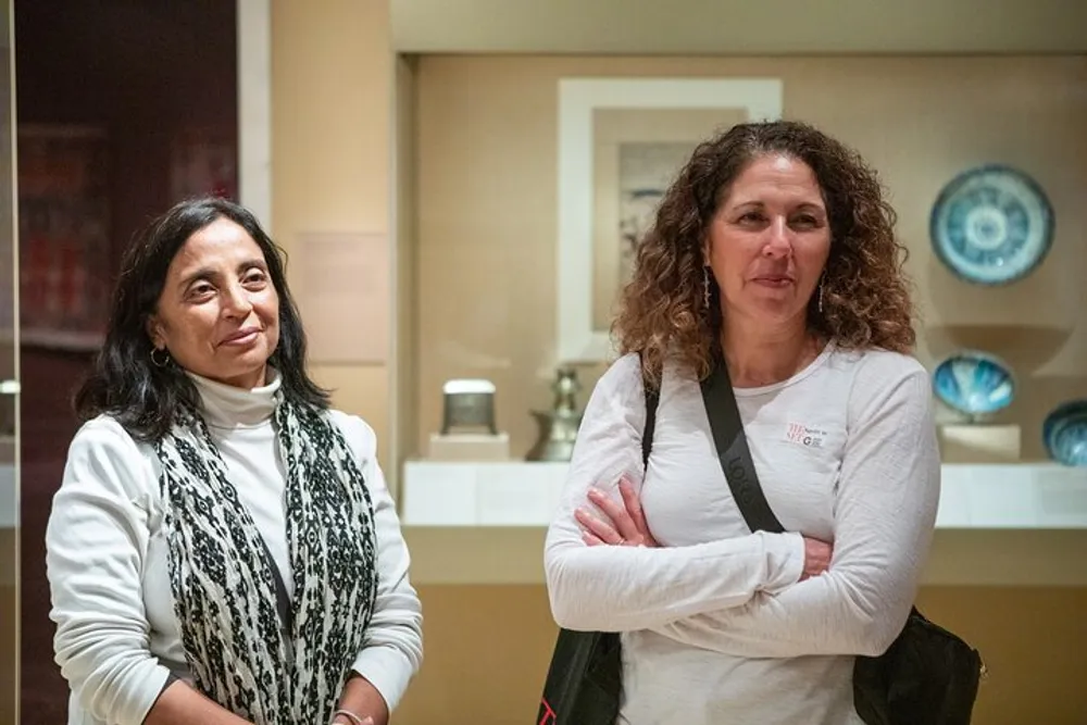 Two women are standing in front of a museum display case seemingly engaged in observing the exhibits or listening to a presentation