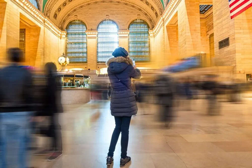 A person stands still in a bustling train station capturing the motion around them