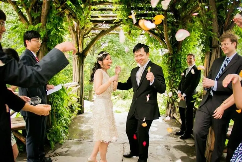 A joyful couple walks through an archway as guests throw flower petals to celebrate their wedding