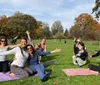 A group of people is participating in an outdoor yoga class in a park filled with trees and enjoying the sunny weather