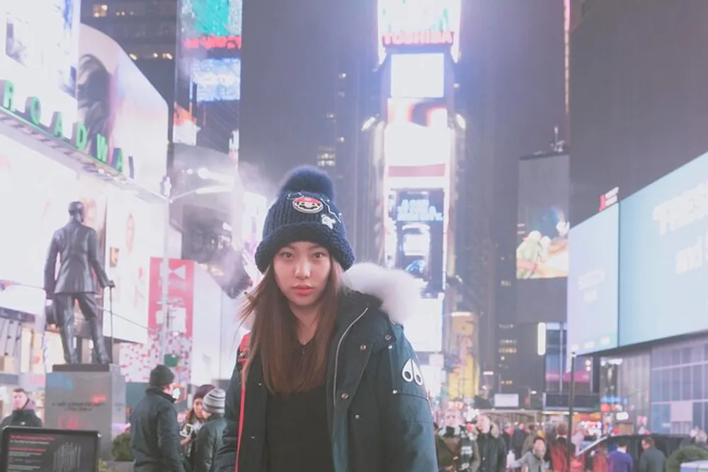 A person is standing in Times Square at night with brightly lit billboards in the background and a crowd of people around