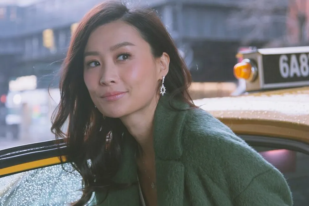 A woman in a green coat is smiling near a yellow taxi with raindrops visible on its surface