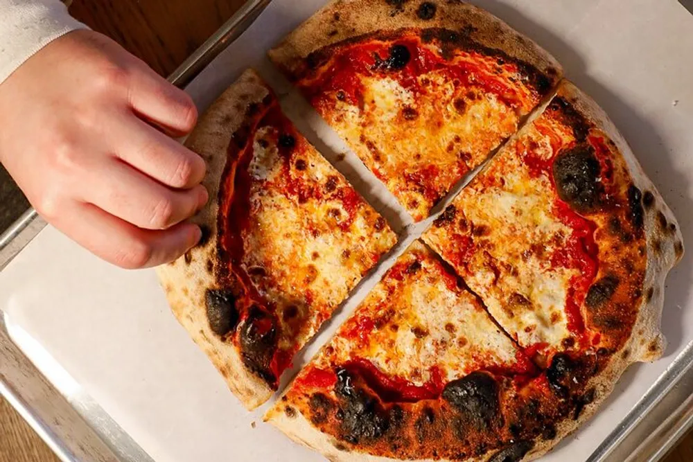 A person is slicing a freshly baked pizza into quarters on a metal tray