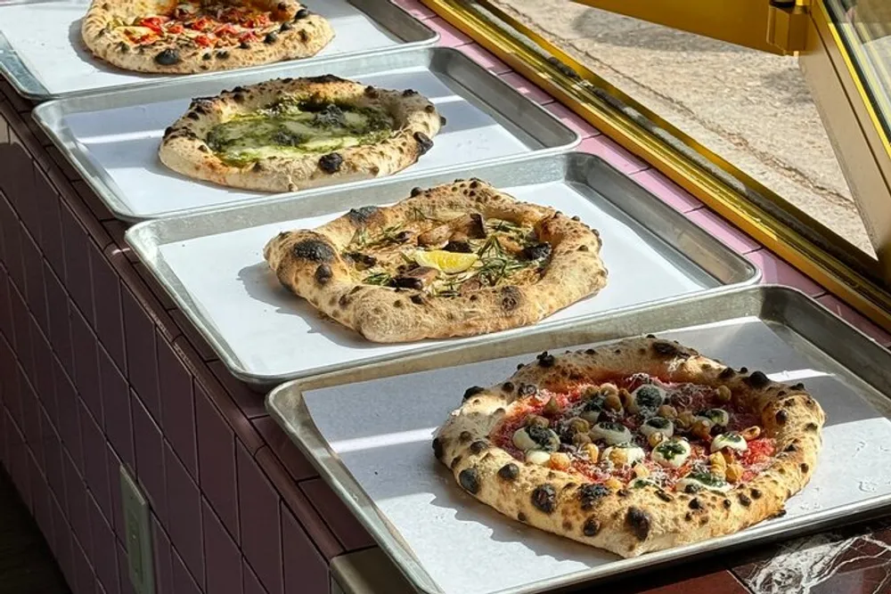 A variety of freshly baked pizzas are on display in a sunlit window showcasing different toppings