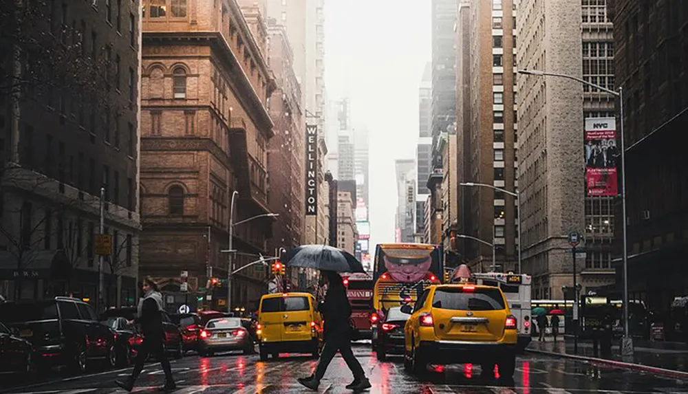 Pedestrians with umbrellas and yellow cabs navigate through a rain-soaked street in a bustling city