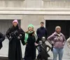 A group of people is standing around the Fearless Girl statue each adopting a similar pose with their hands on their hips emulating the statues confident stance