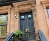 A group of smiling people poses for a photo on the sidewalk in front of a row of brownstone buildings indicative of an urban residential neighborhood