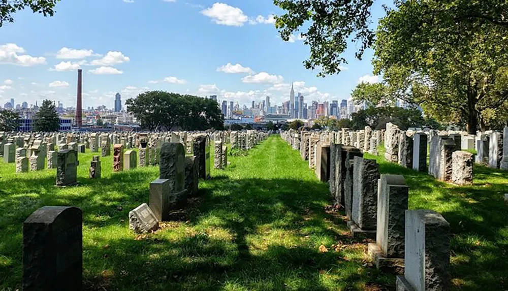 A cemetery with rows of tombstones stretches towards a distant city skyline under a sunny partly cloudy sky