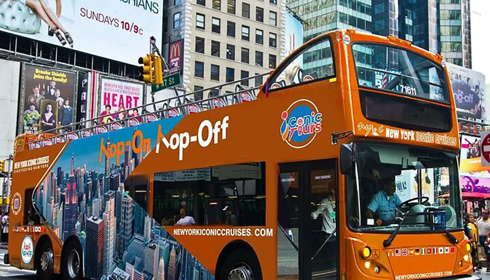 An orange double-decker sightseeing bus with Hop On Hop-Off text is navigating through a bustling urban street with advertising billboards in the background